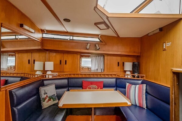 Una cabaña con interior de madera, una mesa central y zonas de estar con cojines azules.