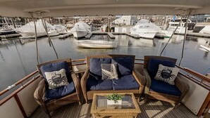 A deck with wicker furniture and cushions, overlooking a marina with boats. - Spacious & Comfy 2BR/2Bath Yacht -Toasty Heat- On Freedom Trail-Walk to Downtown (Boston)