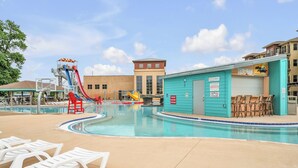 A swimming pool area with a water slide, lounge chairs, and a building with a sign.