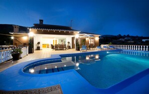 A poolside area with a covered seating area, a pool, and a view of the surrounding landscape.