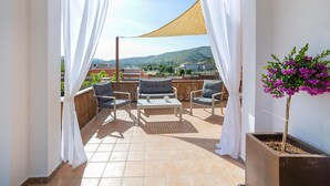 Een balkon met uitzicht op een bergachtig landschap, voorzien van een bank, stoelen en een tafel.