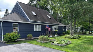 Ein zweistöckiges Haus mit dunkelblauer Fassade, einem geneigten Dach und einer Veranda mit einer kleinen amerikanischen Flagge.