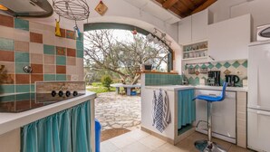Una cocina con suelo de piedra, una estufa a gas, un lavamanos y una silla azul.