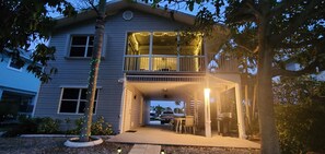 A two-story house with a covered front porch, a balcony with string lights, and a garage with a bicycle. - Direct water access to Charlotte Harbor and Gulf of Mexico with no bridges. (Bokeelia)