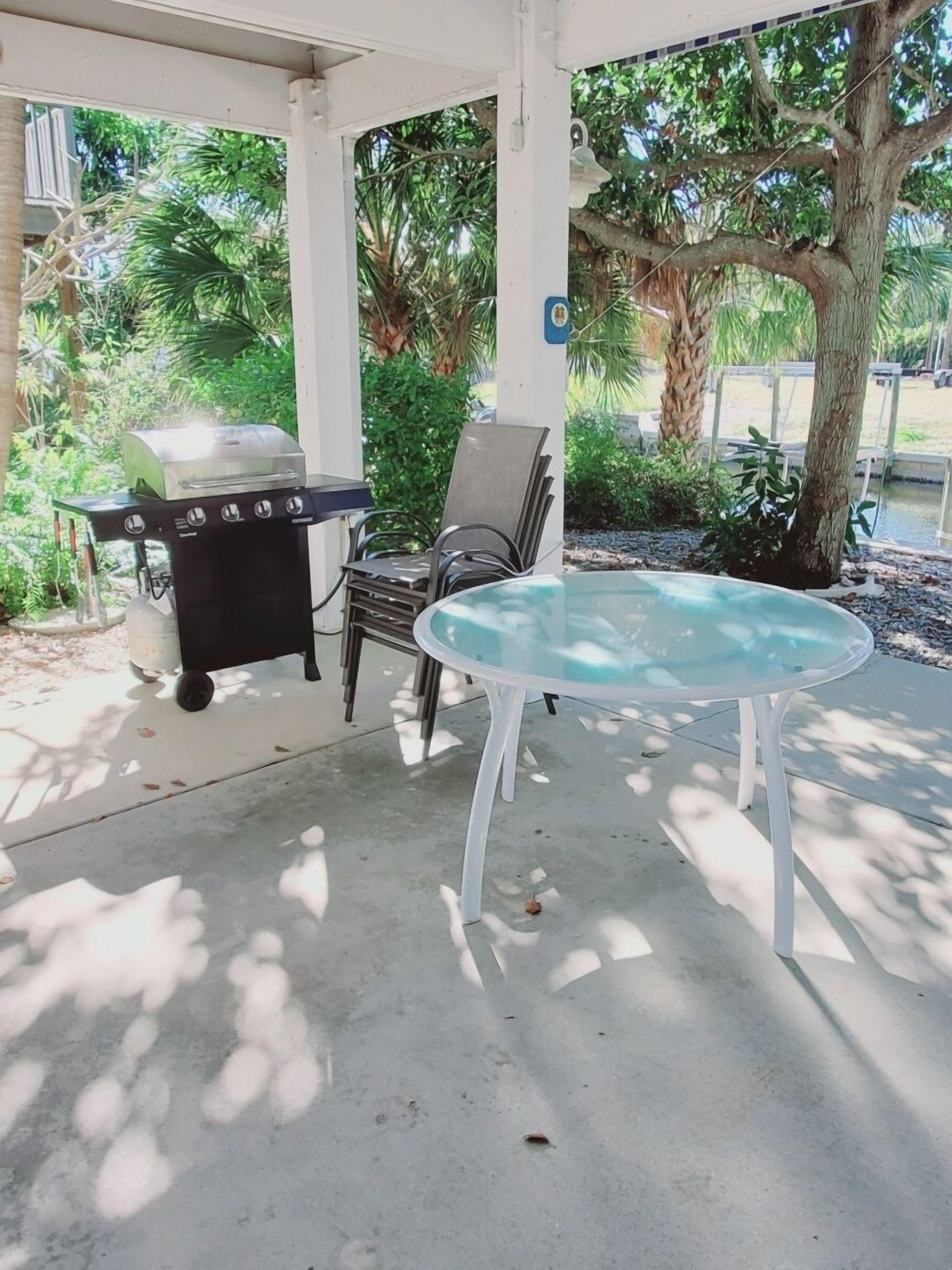 An outdoor patio with a grill, a glass table, and chairs.