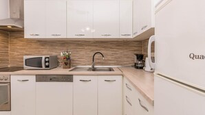 Una cocina moderna con armarios blancos, microondas, lavavajillas, pileta y refrigerador.
