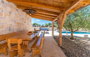 An outdoor patio with a stone wall, wooden benches, a ping pong table, and a pool in the background.