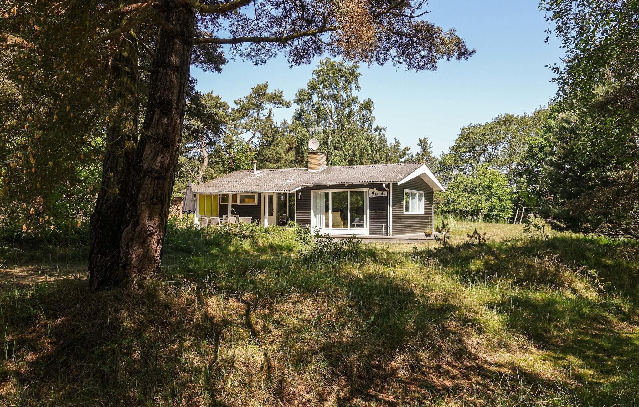 A small, single-story house with a porch, surrounded by trees and grass.