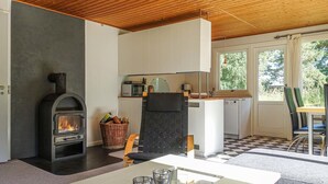A modern kitchen with a wood-burning stove, a dining area with a table and chairs, and a view of the outdoors through large windows. - 2 bedroom stunning home in Aakirkeby (Aakirkeby)