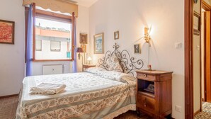 Ein Schlafzimmer mit Bett, Nachttisch, Kommode und einem Fenster mit Vorhängen.