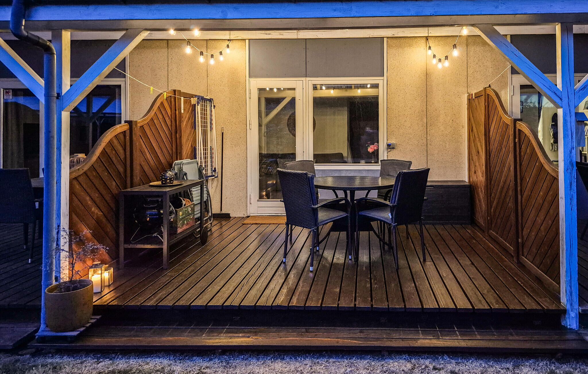 An outdoor patio with a wooden deck, a round table with chairs, and string lights.