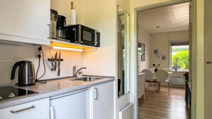 Una cucina compatta con forno a microonde, bollitore e tagliere. Si intravede, attraverso una porta aperta, un'area pranzo con tavolo e sedie.