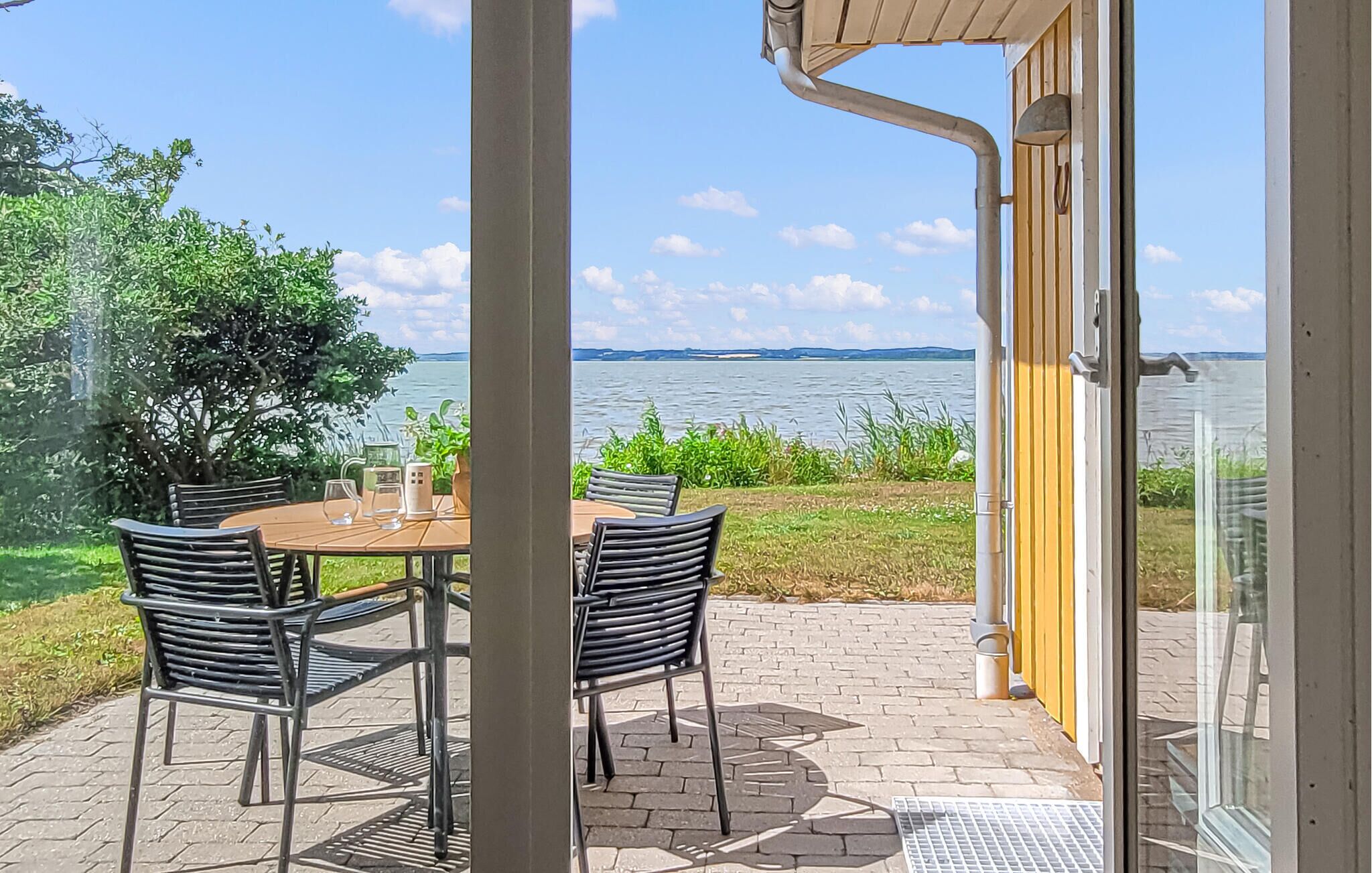 A patio with a table and chairs, a view of a lake, and a building entrance.