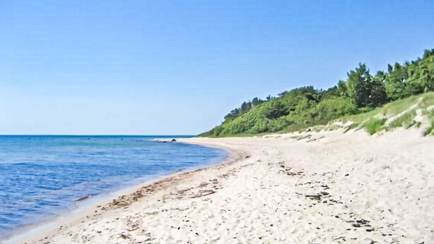 A beach with clear blue water, sandy shore, and green vegetation on the hillside. - Awesome home in Aakirkeby with kitchen (Aakirkeby)