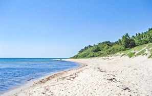 A beach with clear blue water, sandy shore, and green vegetation on the hillside.