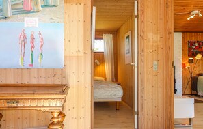 A wooden room with a bed, a desk, and a painting of two figures.