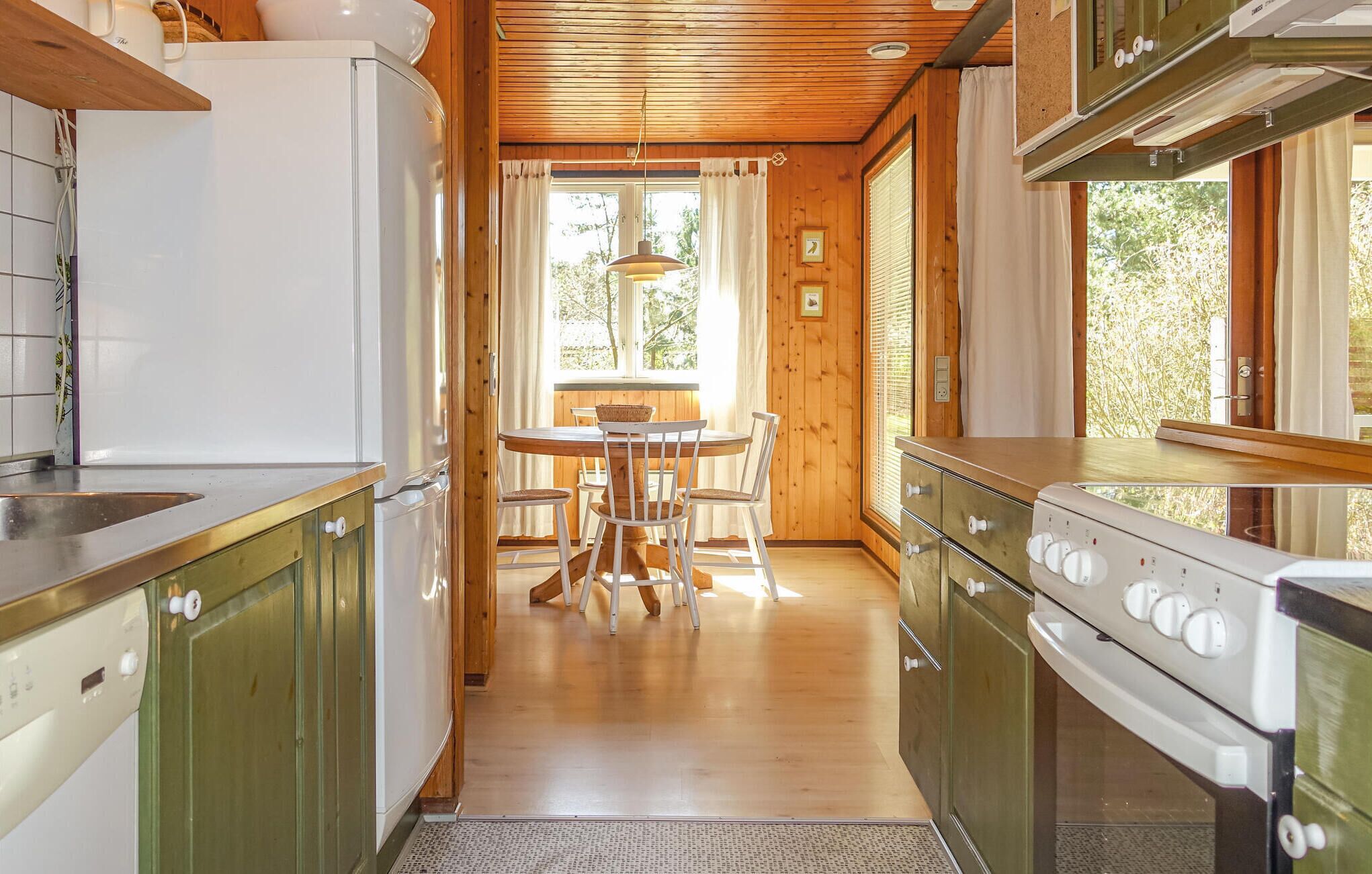 Een keuken met houten kastjes, een fornuis en een eethoek met een tafel en stoelen.