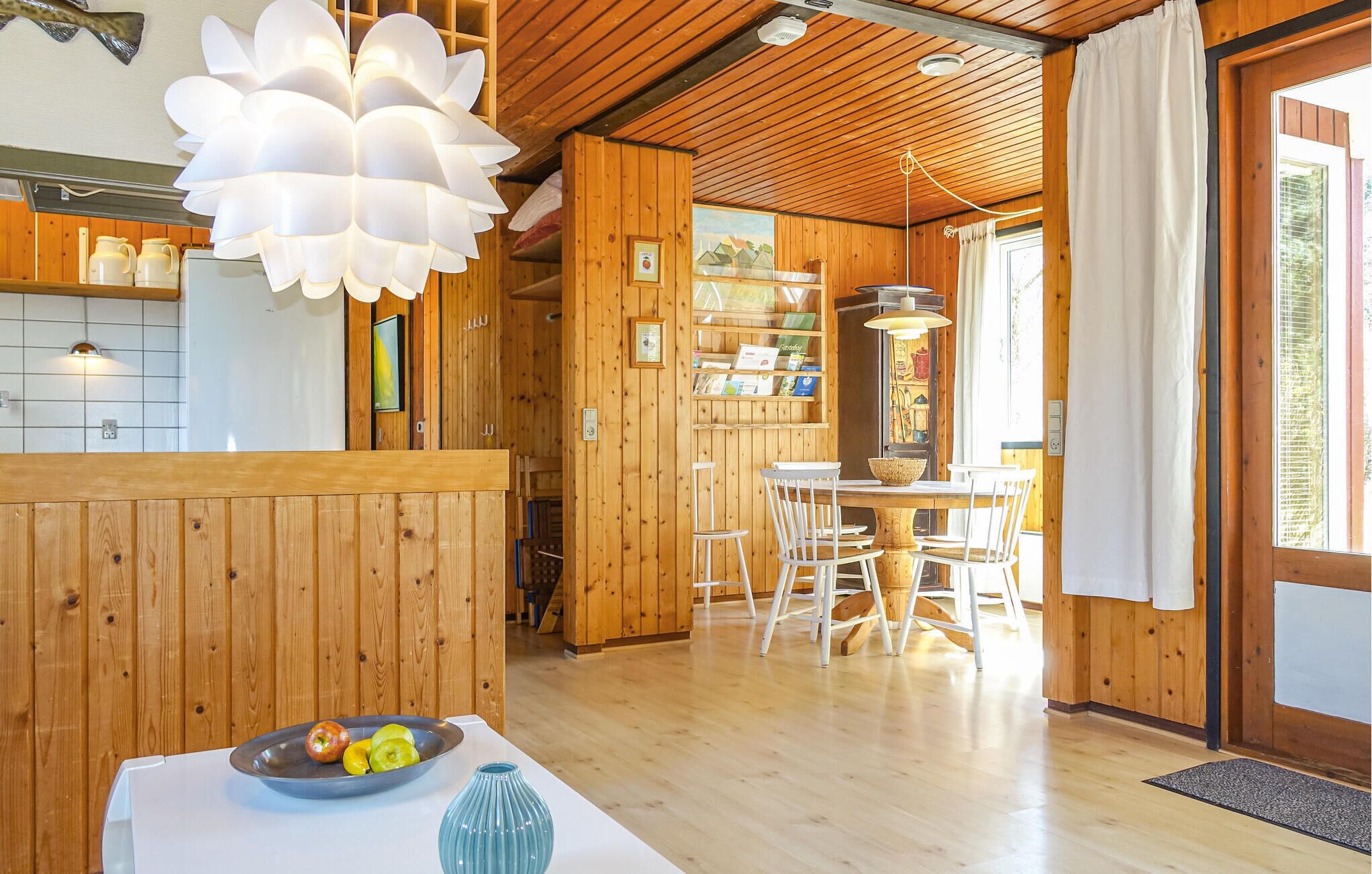 L’intérieur d’un chalet en bois comprend un coin repas, un grand luminaire suspendu blanc et une vue sur l’extérieur par une fenêtre.