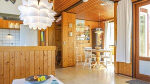 A wooden cabin interior with a dining area, a large white pendant light, and a view of the outdoors through a window. - Awesome home in Aakirkeby with kitchen (Aakirkeby)