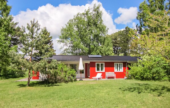 A red house with a white porch, a bench, and a lawn.
