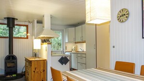 A cozy kitchen with a wood stove, a dining table with chairs, and a clock on the wall. - Amazing home in Nexø with WiFi (Nexø)
