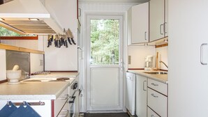 A compact kitchen with white cabinets, a sink, a coffee maker, and a window with a view of trees. - Amazing home in Nexø with WiFi (Nexø)