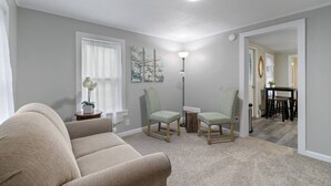 Un salon avec un canapé beige, deux fauteuils verts, un lampadaire et un tableau accroché au mur.