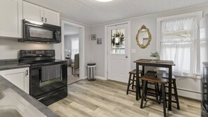Une cuisine équipée d’une cuisinière, d’un four à micro-ondes et d’un four traditionnel. On y trouve une table à manger avec des chaises et une poubelle.
