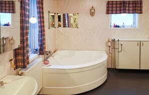 Un baño con una bañera grande, inodoro, lavamanos, espejo y ventana con cortinas.
