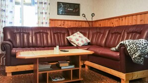 Un salon avec un canapé en cuir marron, une table basse en bois sur laquelle sont posés des livres et des rideaux à motifs.