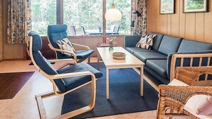 A room with a sofa, two chairs, a table, and a wicker chair.