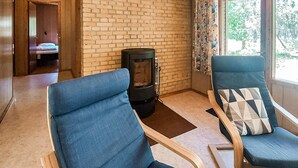 A room with a brick wall, a wood-burning stove, two blue chairs, and a bed in the background.