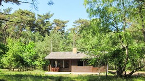A small cabin with a wooden exterior, a porch with chairs, and a chimney.