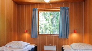 A cabin room with two beds, a window with curtains, and a small desk.