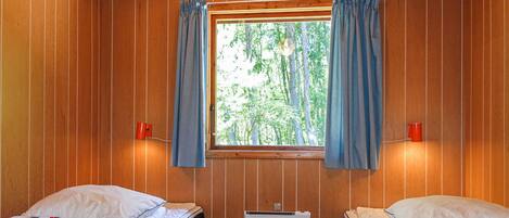 Una habitación tipo cabaña con dos camas, una ventana con cortinas y un escritorio pequeño.