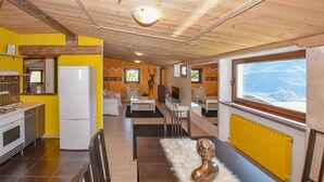 A compact kitchen with a refrigerator, stove, and sink. There is a dining area with a table and chairs, and a large window offering a view of a snowy landscape. - Cozy apartment in Verrayes with sauna (Verrayes)