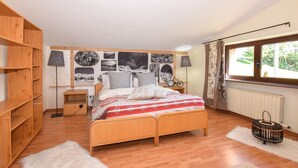 A bedroom with a wooden bed, a bookshelf, a wall with photographs, a window with curtains, and a radiator. - Cozy apartment in Verrayes with sauna (Verrayes)