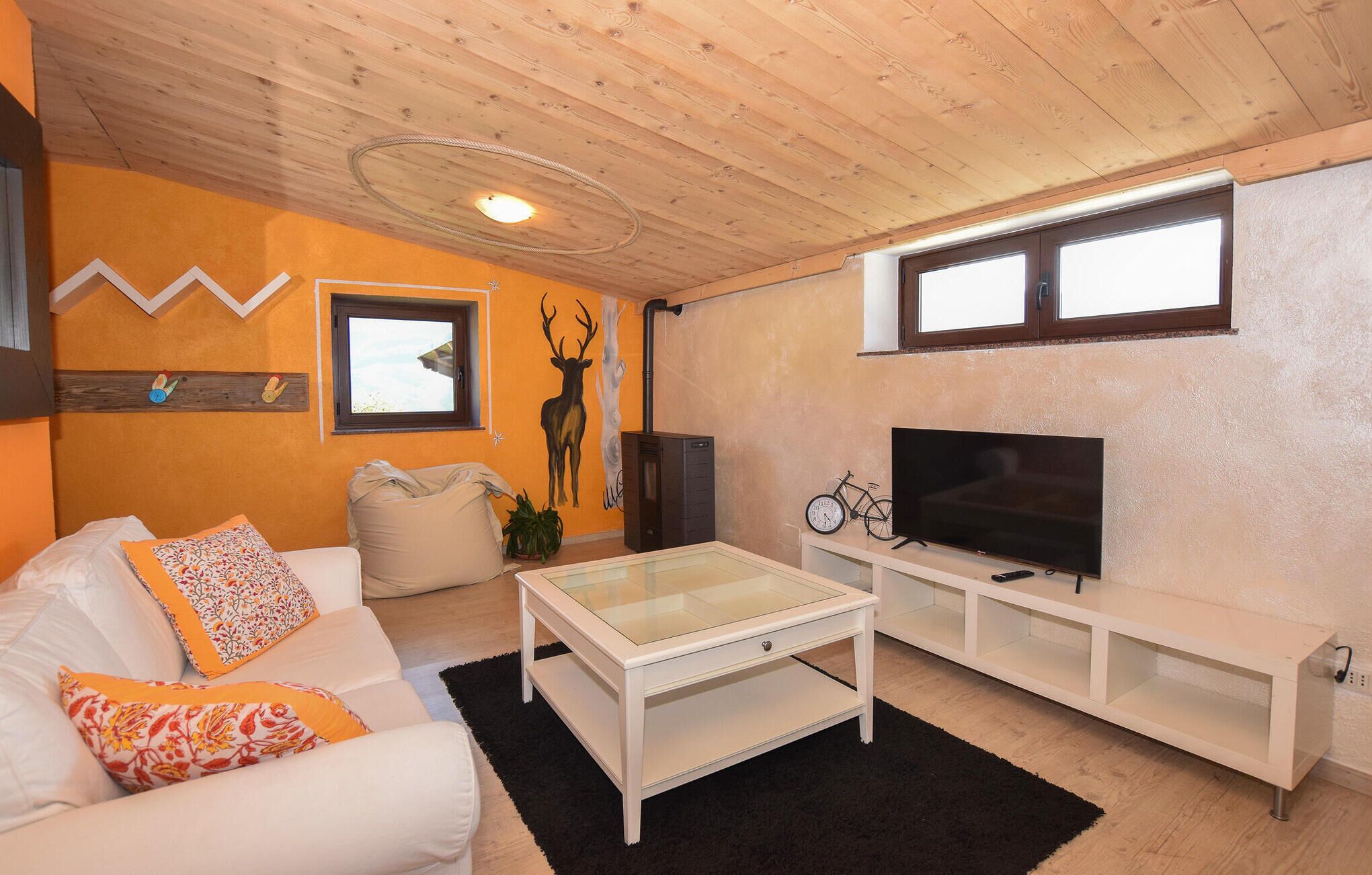 Een gezellige woonkamer met een witte bank, een glazen salontafel, een televisie op een witte kast, en een houten plafond.