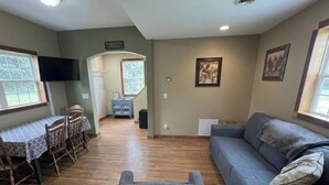 A living room with a gray sofa, wooden dining table with chairs, a TV mounted on the wall, and a framed picture. - 2 Bedrooms - Room to park boat! - Close to water & Potawatomi State Park (Sturgeon Bay)