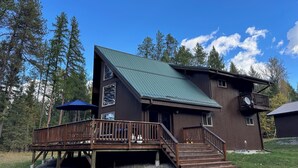 A two-story wooden cabin with a green metal roof, a wooden deck, and a satellite dish.