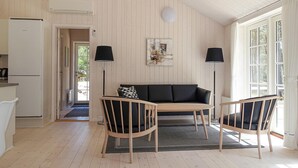 Ett mysigt rum med trägolv, en svart soffa, två trästolar, ett litet bord och en tavla på väggen.
