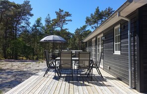 Eine Holzterrasse mit Tisch, Stühlen und Sonnenschirm, sowie ein Gebäude mit Fenstern.