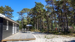 En stuga med en träveranda, utomhusmöbler och en skog som bakgrund.