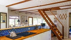 Eine Küche mit Holzausziehtisch, blauen Fliesen an der Rückwand, weißen Schränken und einer Holztreppe.