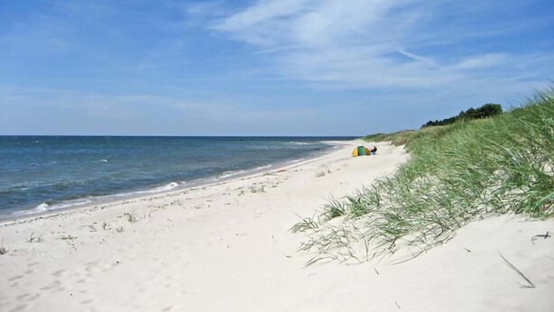 A beach with white sand, a clear blue sky, and a calm sea. There are tents set up on the sand.