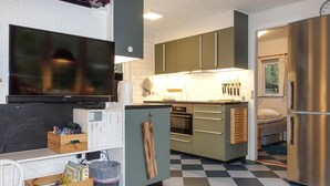 A compact kitchen with a TV, wooden cabinets, a built-in oven, and a stainless steel refrigerator.