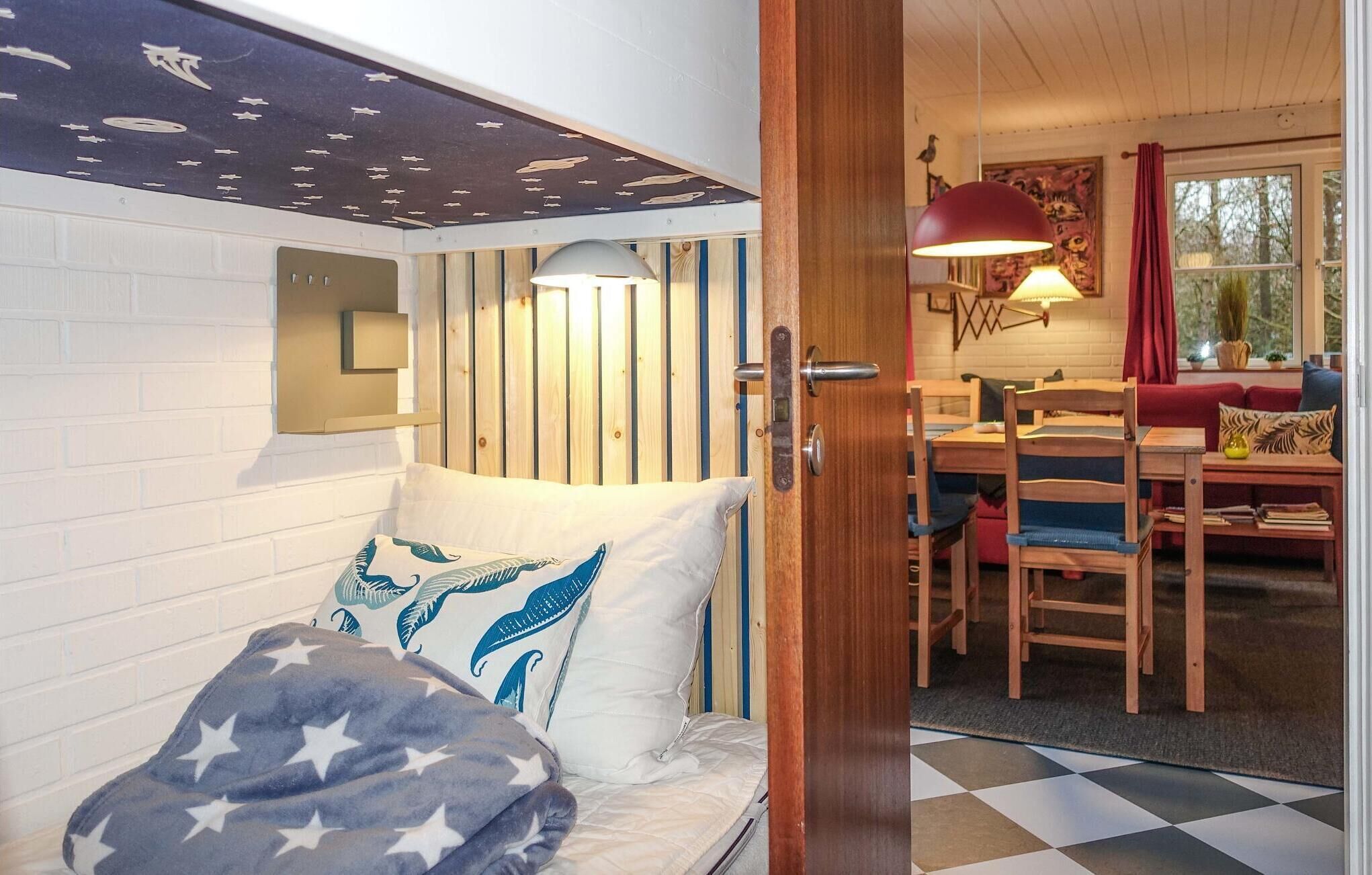 Een knus ingerichte kamer met een bed, een houten hoofdbord, een wandlamp, een eettafel met stoelen en uitzicht op het buitenlands landschap door een raam.