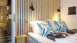 A bedroom with a wooden slat wall, a bed with white bedding and blue leaf-patterned pillows, and two wall-mounted reading lamps.