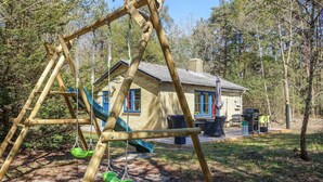 A wooden swing set in a wooded area with a small cabin in the background.