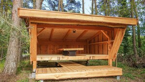 A wooden cabin with a bench and a table, surrounded by trees.